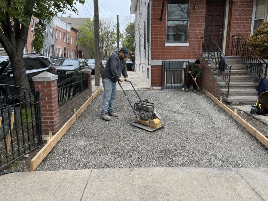 Crew compacting a crushed-stone base for a concrete driveway in Brooklyn